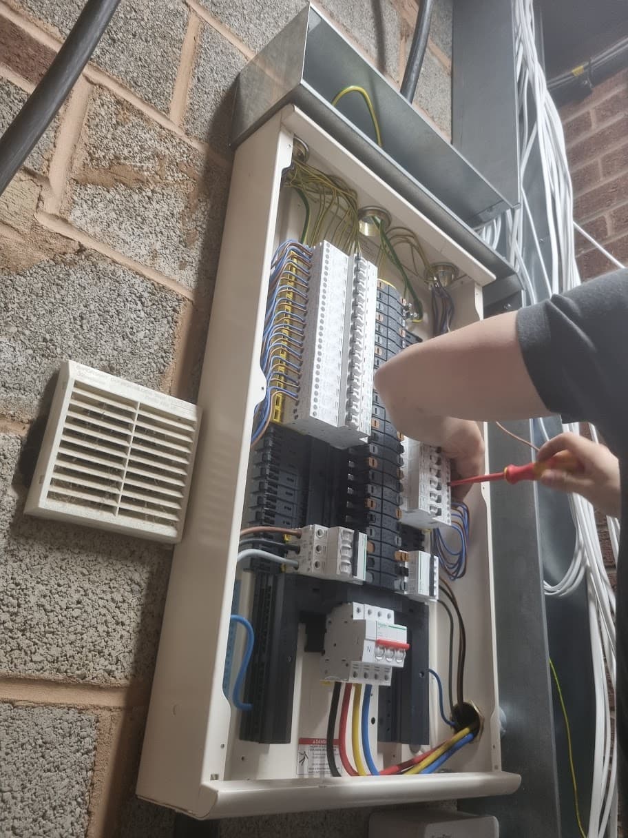 Schneider Acti9 three-phase distribution board installed during a commercial rewire in Cannock, shown with an engineer connecting circuits inside the open enclosure.