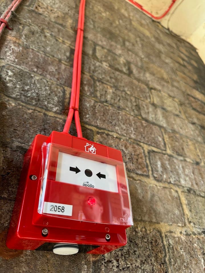 Close-up of an installed Apollo manual call point at Erdington Fire Station, wall-mounted with fire alarm cabling connected above.