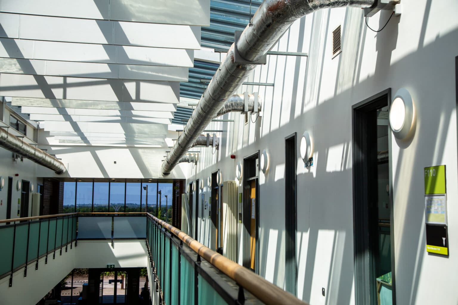 A first-floor circulation walkway at The Foster Centre fitted with new circular LED wall luminaires, overlooking the entrance area below.