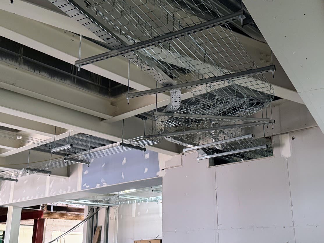 Electrical containment and cable basket installation within an exposed ceiling void at Nuneaton Digital Skills Centre, coordinated around structural steelwork.
