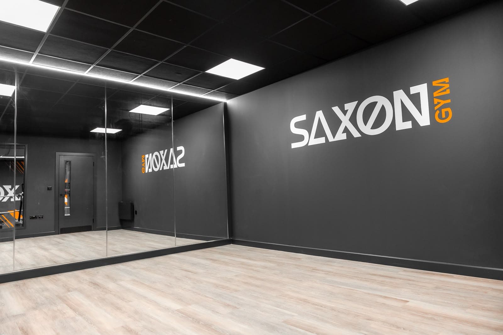 Mirrored studio room at Saxon Gym in Cannock, with a continuous linear accent light above the full-height mirrors and recessed LED panels in the black suspended ceiling.