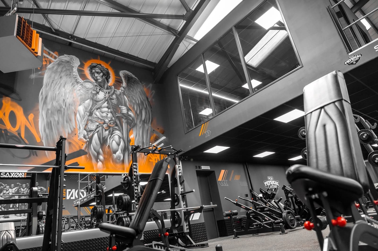 Mezzanine level at Saxon Gym in Cannock, with glazed windows overlooking the gym floor, LED panel lighting to the underside of the mezzanine and a large painted mural on the adjacent wall.