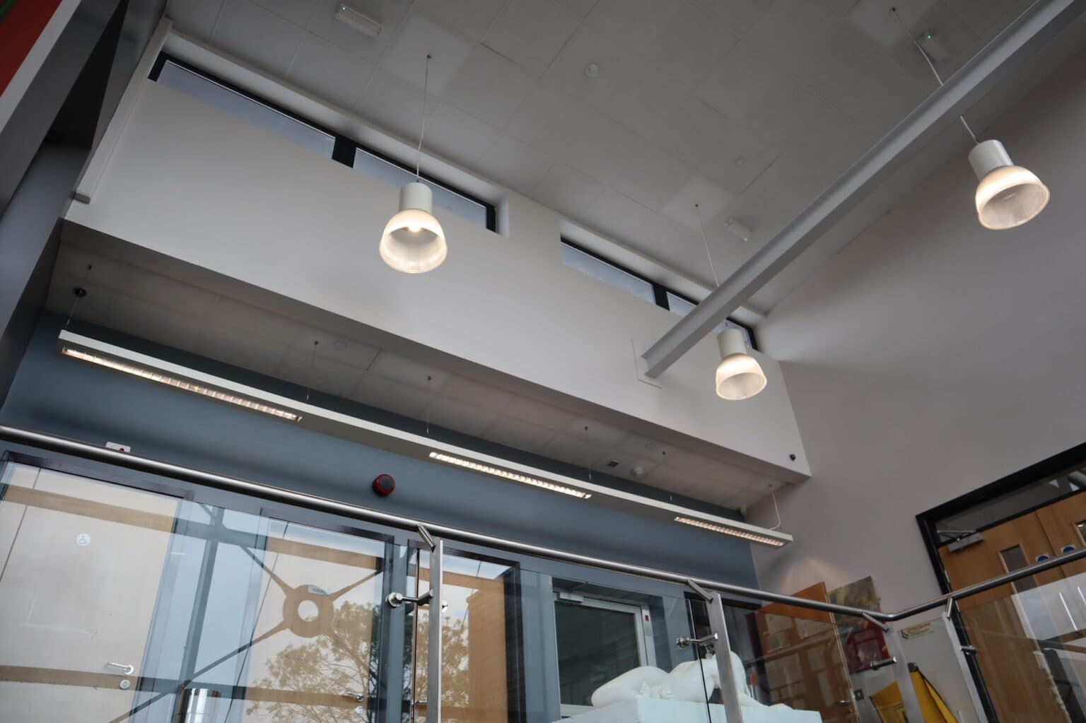 New LED linear pendant fittings installed above a corridor and stairwell at Stoke Park School, illuminating doors to toilets, a cleaners' store and a fire exit.