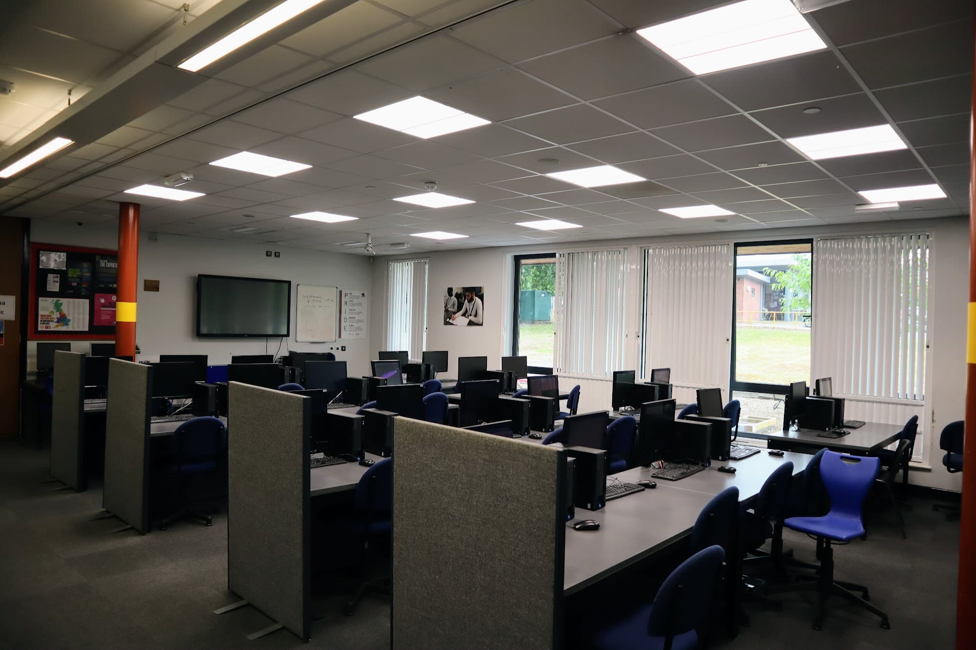 A refurbished IT suite at Stoke Park School fitted with new recessed LED ceiling panels, showing rows of computer workstations with partition screens.