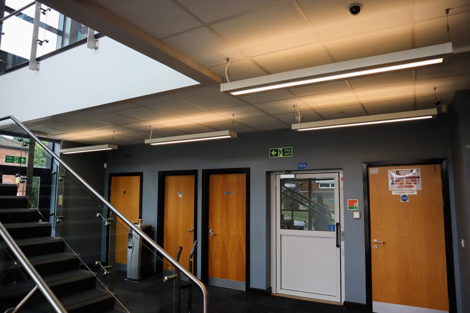 New LED pendant and linear lighting installed in a double-height reception area at Stoke Park School, with glazed entrance doors and a stairwell visible below.