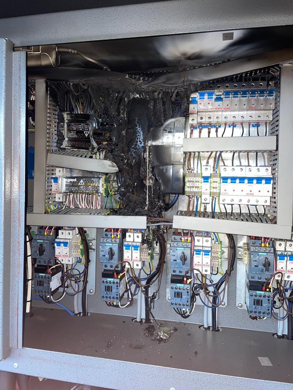 Severe fire damage inside a commercial distribution board, with melted cabling and charring across the enclosure — the kind of finding recorded as C1, danger present, on an EICR.