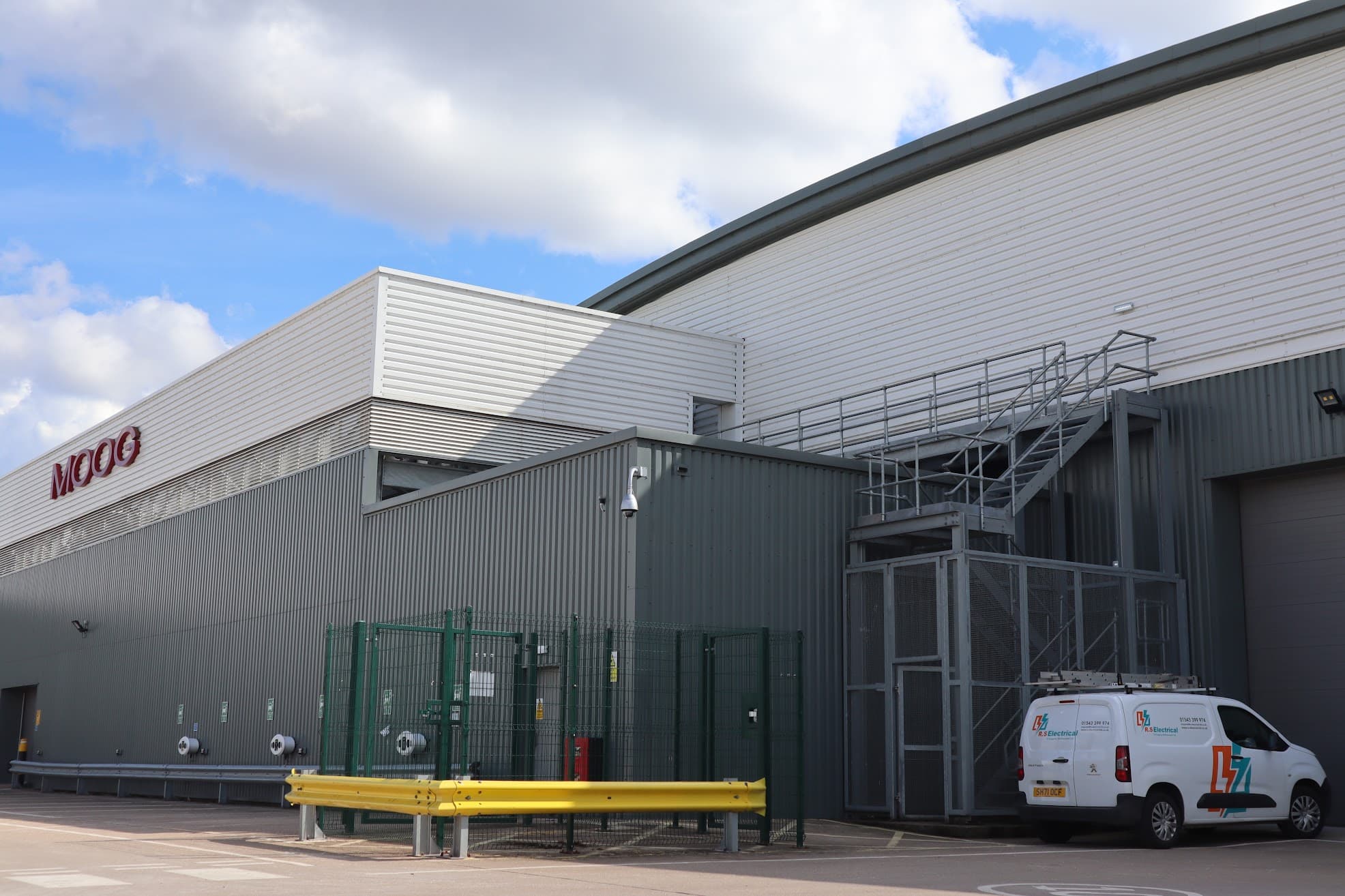 An RS Electrical van parked outside a large industrial facility, with an external access platform and stairway visible on the building.