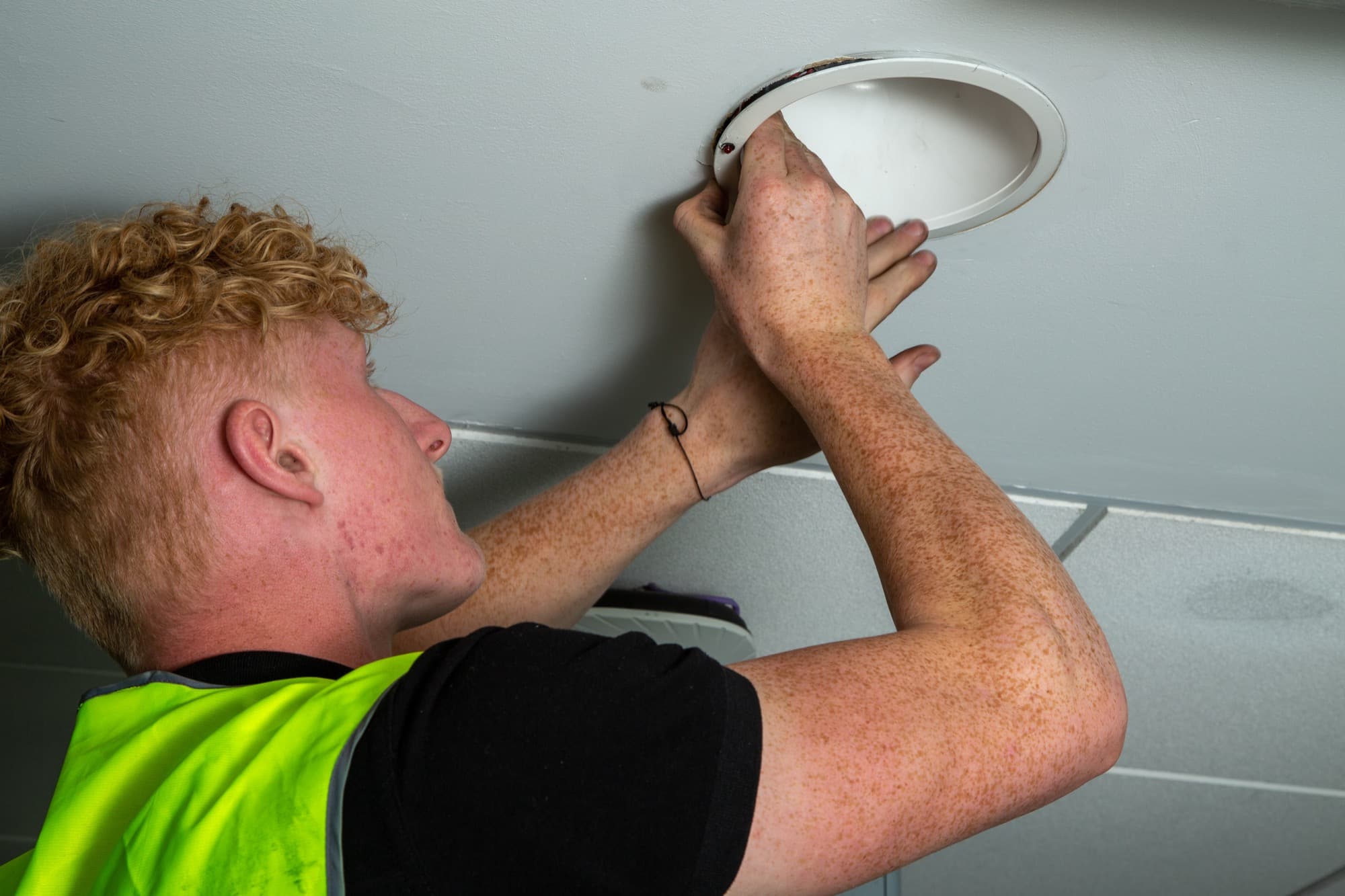 Close-up of an RS Electrical engineer in hi-vis workwear fitting a recessed LED downlight into a suspended ceiling tile.