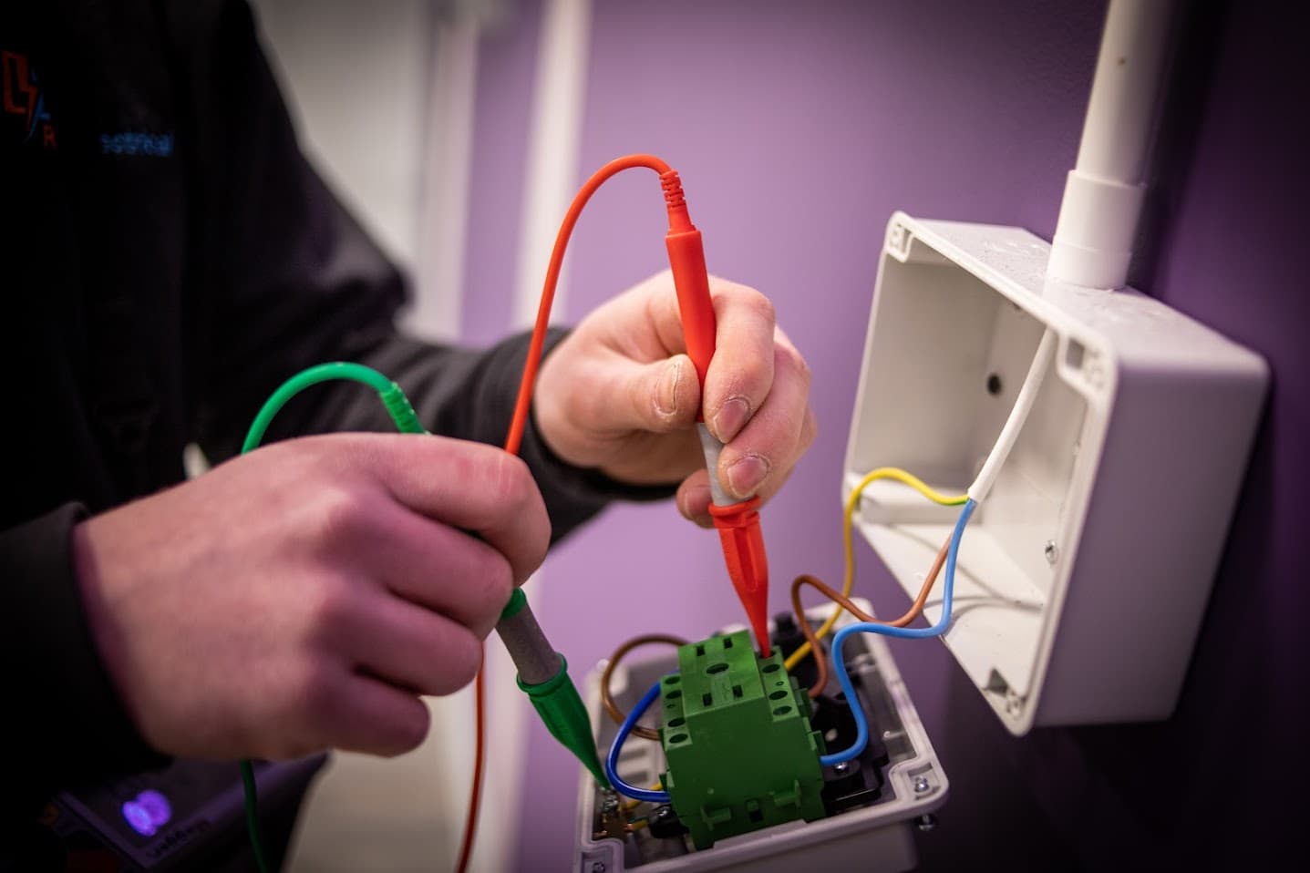 An RS Electrical engineer taking a reading with two test probes inside an open wall-mounted enclosure during a commercial inspection.